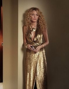 a woman with long blonde hair wearing a gold dress and holding a cell phone in her hand