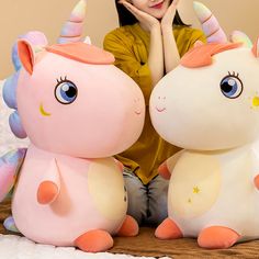 a woman sitting next to two stuffed unicorns