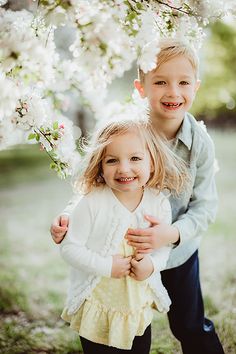 two young children standing under a tree with white flowers