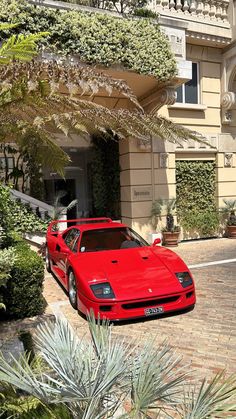 a red sports car parked in front of a large building with trees and bushes around it