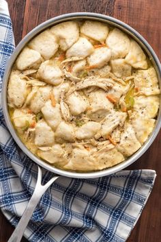 a pot filled with chicken and dumplings on top of a blue napkin next to a fork