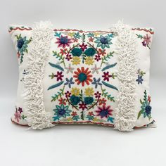 an embroidered pillow with tassels and flowers on the front, sitting on a white surface