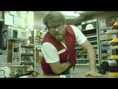 a man with glasses and a red vest leaning on a counter in a store looking at the camera