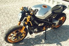 a silver and gold motorcycle parked on top of a cobblestone road