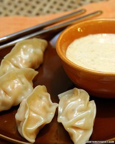 dumplings on a plate with dipping sauce in a bowl next to chopsticks