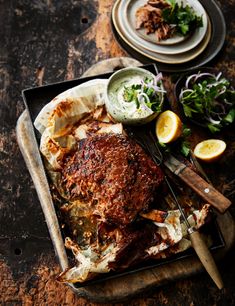 a roasting pan filled with meat, vegetables and sauces on a wooden table