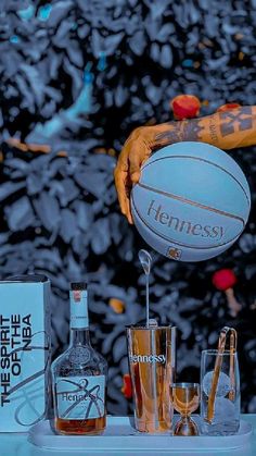 a person is holding a basketball above glasses and liquor bottles on a table with an advertisement in the background