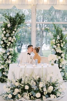 a bride and groom kissing in front of an archway decorated with white flowers at their wedding reception