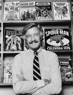 a man standing in front of a book shelf filled with comic books and covers on it