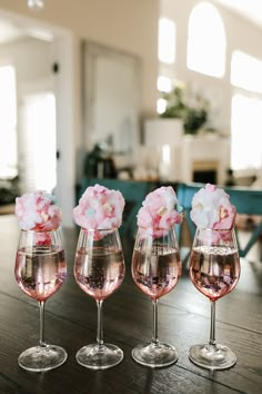 three wine glasses filled with pink flowers on top of a wooden table in a living room