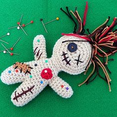 a crocheted doll laying on top of a green surface next to pins and needles