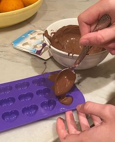 two hands scooping chocolate from a muffin pan into a bowl with oranges in the background