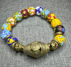 a gold bracelet with multi colored beads and an elephant head on the clasp is sitting on a gray surface