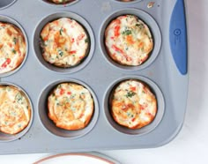 a muffin tin filled with mini pizzas on top of a white countertop