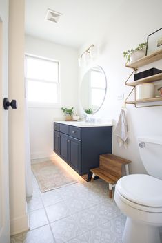 a white toilet sitting in a bathroom next to a wooden shelf filled with books and plants