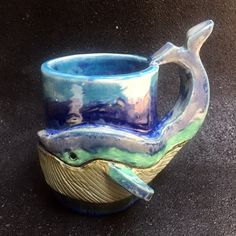 a ceramic mug with a whale on it's side sitting on a black surface