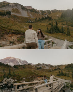 two people standing on a bridge in the mountains, one is taking pictures with his camera