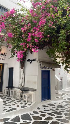 a white building with purple flowers growing over it's door and windows on the side