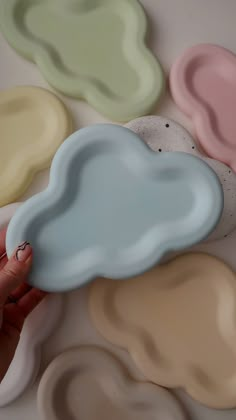 a hand holding a cloud shaped object in front of several different colored clouds on a white surface