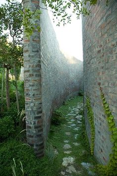 an alley between two brick buildings with green plants growing on the walls and walkways