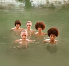 four people are in the water with their backs turned to the camera and one person is wearing no shirt