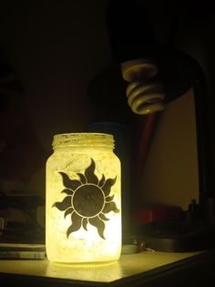 a mason jar sitting on top of a wooden table next to a light that is turned on