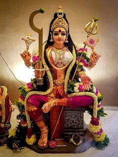 a statue of the hindu god sitting on top of a chair with two candles in his hand