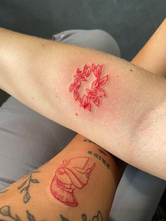 two people with tattoos on their arms, one has a red tattoo and the other has a bell