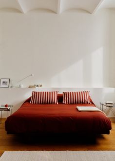 a bed with red sheets and pillows in a white room