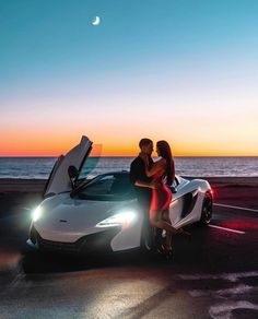 two people sitting on the hood of a white sports car with their hands in the open doors