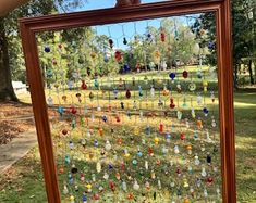 a person is holding up a framed glass art piece in front of a grassy field