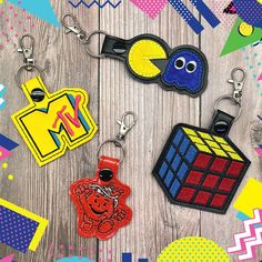 four different keychains are shown on a wooden surface with colorful shapes and colors