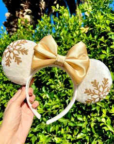 a hand holding up a gold and white snowflake mouse ears with a bow