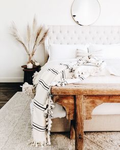 a bed with white linens and pillows on it, next to a wooden table