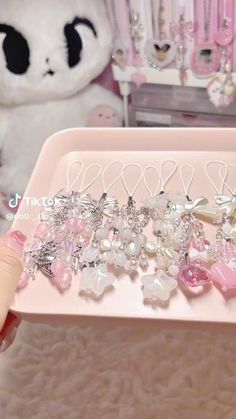 a pink tray holding several pairs of earrings and a white teddy bear in the background