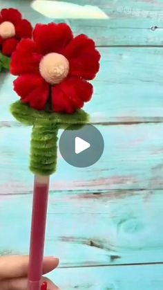 someone is holding a flower made out of toothpick and yarn with red flowers on it