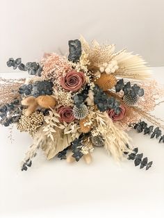 an arrangement of dried flowers and foliage on a white surface