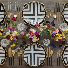 the table is set with black and white plates, gold cutlery, floral centerpieces, and colorful flowers