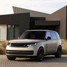 a silver range rover parked in front of a modern house with grass and shrubs around it