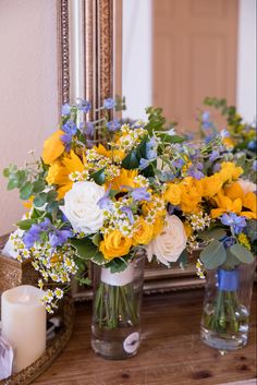 two vases filled with yellow and white flowers sitting on a table next to a mirror