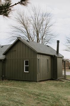 a small green building sitting on top of a grass covered field next to a tree