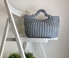 a crocheted bag sitting on top of a white shelf next to a potted plant