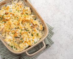 a casserole dish with chicken, cheese and parsley on a striped towel