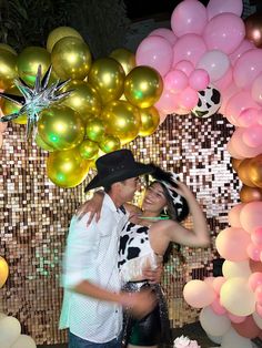 a man and woman standing next to each other in front of balloons