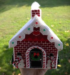 a hand holding up a small red and white house with candy canes on it