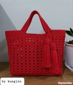 a red crocheted bag sitting on top of a table next to a potted plant