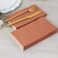 two brown notebooks with gold forks and knives next to each other on a table