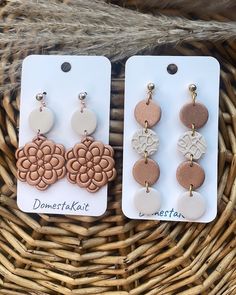 two pairs of wooden earrings with flower designs on them sitting in front of a wicker basket