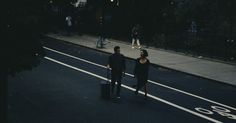 a man and woman walking down the street at night with their suitcases in hand