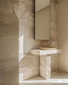 a bathroom sink sitting under a mirror next to a wall mounted faucet on top of a stone counter